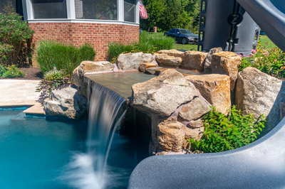 Two-tiered natural stone boulder waterfall cascading into a pool surrounded by lush garden greenery