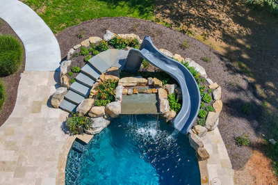 Two-tiered natural stone boulder waterfall cascading into a pool with steps and lush plants