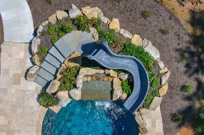 Multi-tiered natural stone waterfall cascading into a pool surrounded by lush garden greenery
