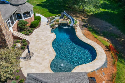 Two-tiered natural stone boulder waterfall cascading into a freeform pool beside a water slide