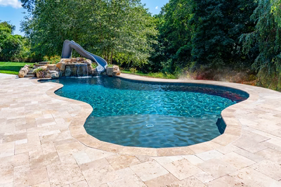 Two-tiered natural stone boulder waterfall cascading into a freeform pool surrounded by lush greenery