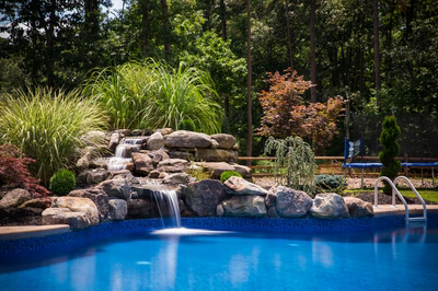 Multi-tiered natural stone boulder waterfall cascading into a blue pool surrounded by lush greenery