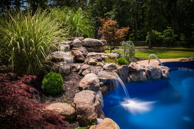 Multi-tiered natural stone boulder waterfall cascading into a pool surrounded by lush garden plants