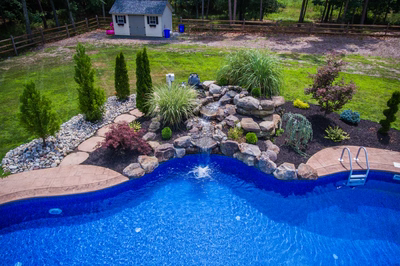 Multi-tiered natural stone boulder waterfall cascading into a blue pool surrounded by lush greenery