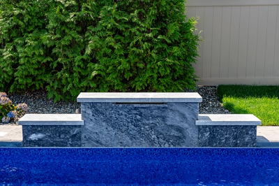 Three-tiered natural stone spillway waterfall cascading into a blue pool bordered by lush hedges