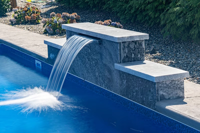 Three-tiered natural stone waterfall cascading into a blue pool with surrounding gravel and plants