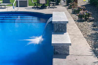 Two-tiered natural stone boulder waterfall cascading into swimming pool bordered by gravel and hydrangeas