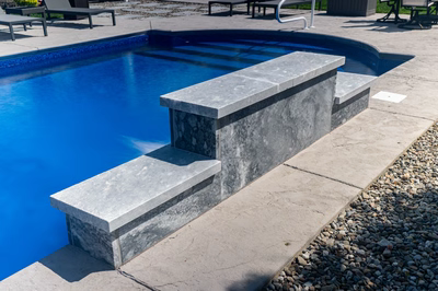 Three-tiered natural stone waterfall feature cascading into a blue pool with a concrete surround
