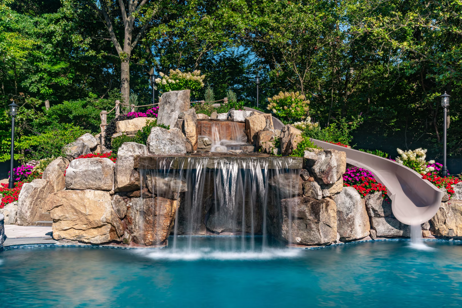 Natural boulder waterfall cascading into a pool surrounded by lush floral landscaping