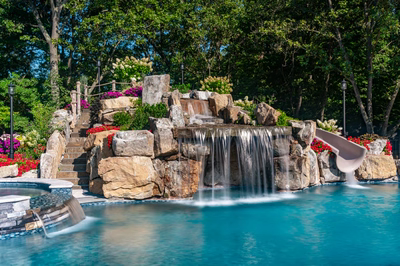 Multi-tiered natural stone boulder waterfall cascading into a pool surrounded by lush garden landscaping