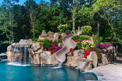 Two-tiered natural stone boulder waterfall cascading into a pool with lush floral landscaping