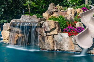 Multi-tiered natural stone boulder waterfall cascading into a pool surrounded by lush floral landscaping