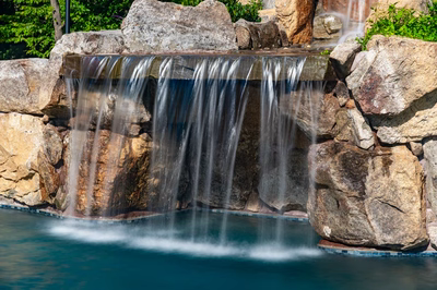 Two-tiered natural stone boulder waterfall cascading into a pool surrounded by lush green plants