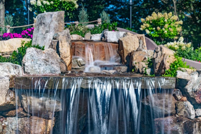 Two-tiered natural stone boulder waterfall cascading into a pool with vibrant floral landscaping