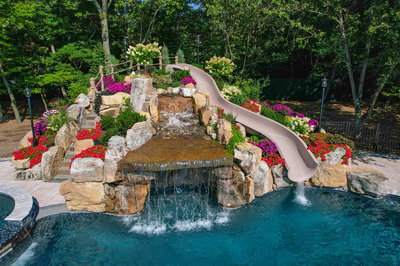 Triple-tiered natural stone boulder waterfall cascading into a pool surrounded by lush, colorful floral landscaping