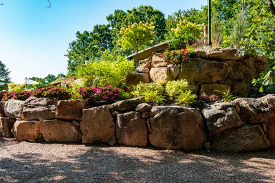 Multi-tiered natural stone boulder waterfall cascading into a pool surrounded by lush garden greenery