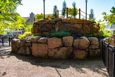 Two-tiered natural stone boulder waterfall cascading into a pool area with lush green plants