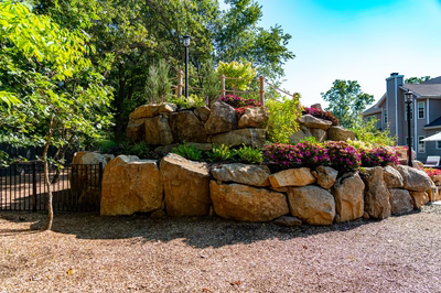 Multi-tiered natural stone boulder waterfall cascading into a pool amidst vibrant garden plants