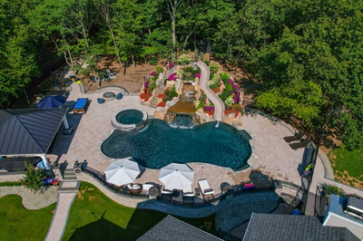 Multi-tiered natural stone boulder waterfall cascading into a freeform pool with lush, colorful landscaping