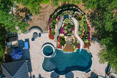Multi-tiered natural stone boulder waterfall cascading into a freeform pool amidst vibrant floral landscaping