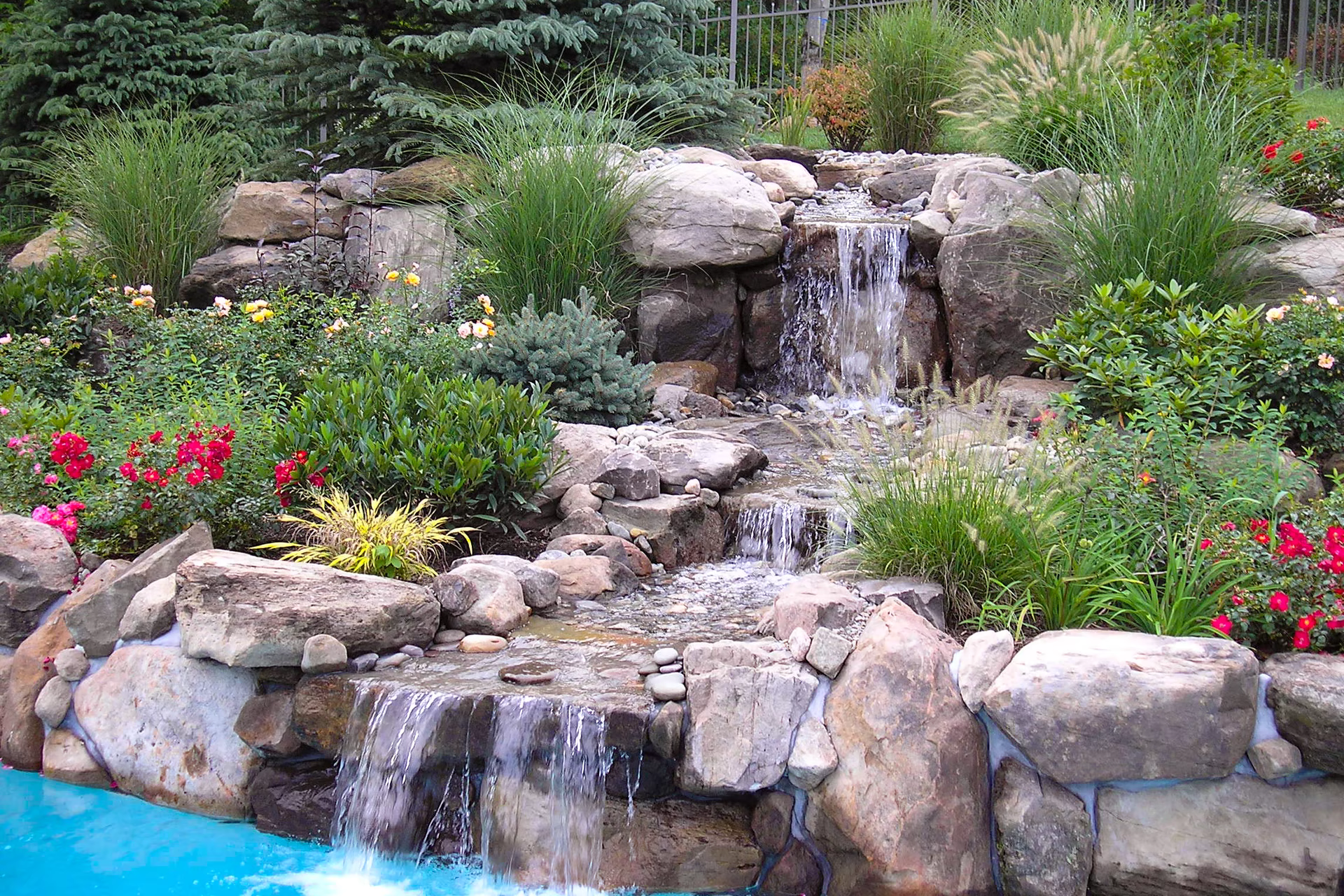 Stepped stone cascade descending tier to tier over a compacted-stone base into the pool