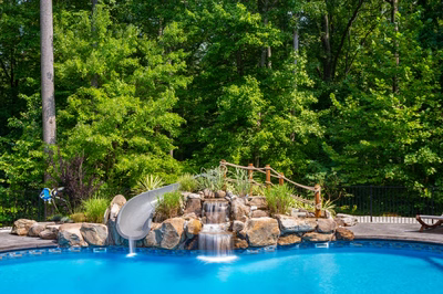 Two-tiered natural stone boulder waterfall cascading into a pool surrounded by lush green trees