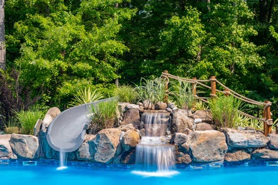 Two-tiered natural stone boulder waterfall cascading into a pool surrounded by lush greenery