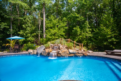 Two-tiered natural stone boulder waterfall cascades into a pool surrounded by lush forest greenery