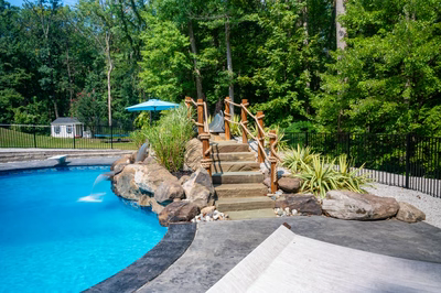 Multi-tiered natural stone boulder waterfall cascading into a freeform pool with lush surrounding greenery