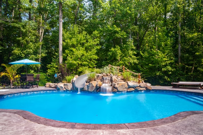 Two-tiered natural stone boulder waterfall cascading into a pool surrounded by lush green trees