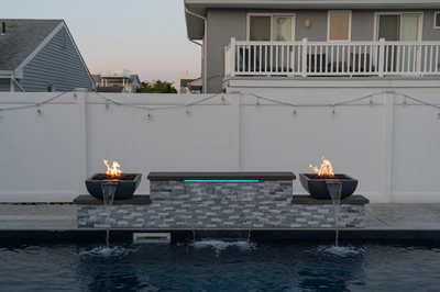 Three-tiered stacked stone wall with fire bowls cascading water into a modern swimming pool