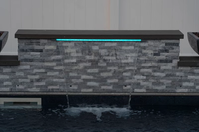 Single-tier LED-lit sheer descent waterfall cascading from a stacked stone wall into a pool