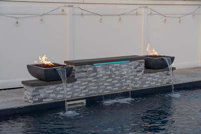 Multi-tiered stone waterfall with fire bowls and sheer descents cascading into a backyard pool
