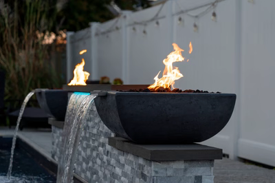 Multi-tiered stone fire bowls cascading water into a pool near a white fence