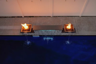 Triple sheer descent waterfalls cascading from a stone wall into a pool with fire bowls