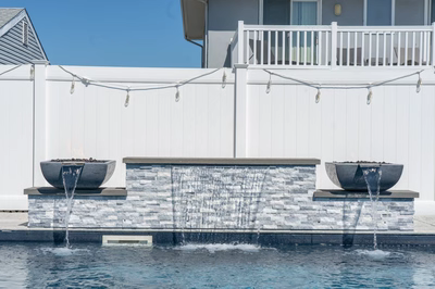 Three-tiered natural stone boulder waterfalls cascading into a swimming pool with white fencing