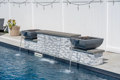 Three-tiered natural stone waterfall cascading into a pool beside a blooming potted plant