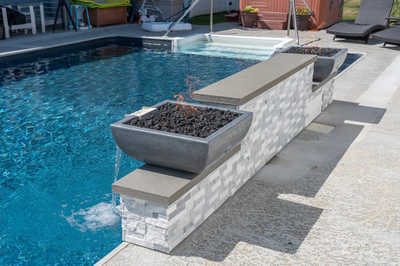 Single-tier stacked stone wall featuring fire bowls cascading water into a backyard swimming pool