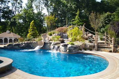 Multi-tiered natural stone boulder waterfalls cascading into a blue pool with lush garden greenery