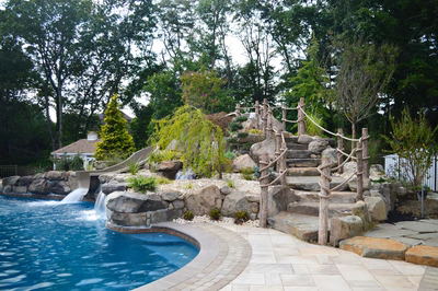 Multi-tiered natural stone boulder waterfall cascading into a pool surrounded by lush garden landscaping