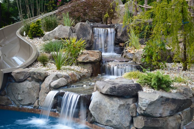 Three-tiered natural stone boulder waterfall cascading into a pool surrounded by lush garden landscaping