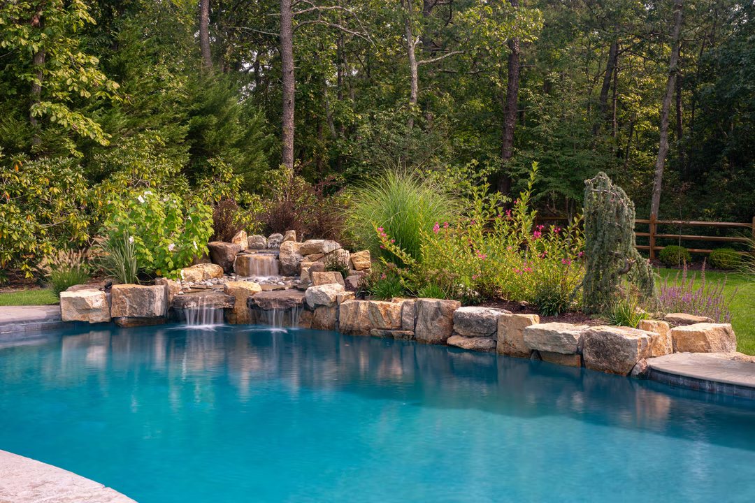 Multi-tiered natural stone boulder waterfall cascading into a pool surrounded by lush garden greenery