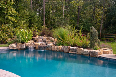 Multi-tiered natural stone boulder waterfall cascading into a pool surrounded by lush garden greenery