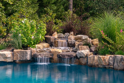 Natural stone boulder waterfalls cascading over multiple tiers into a pool with lush landscaping