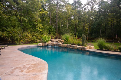 Multi-tiered natural stone boulder waterfall cascading into a freeform pool surrounded by lush greenery