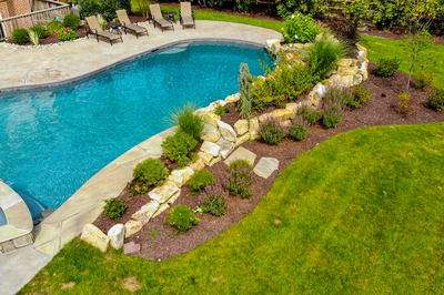 Multi-tiered natural stone boulder waterfall cascading into a pool surrounded by lush garden plants