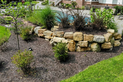 Multi-tiered natural stone boulder waterfall cascading into a pool surrounded by lush garden plants