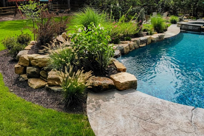 Low-profile natural stone boulder waterfall cascading into a pool bordered by lush ornamental landscaping