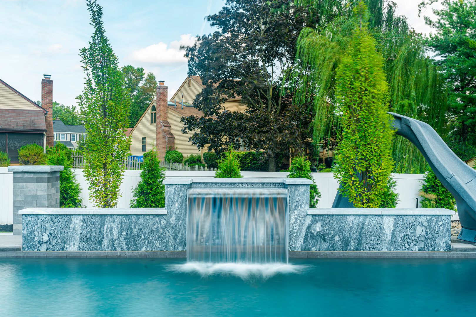 Sheer descent natural stone waterfall cascading into a pool surrounded by lush green landscaping