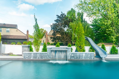 Single-tier natural stone waterfall cascading into a rectangular pool surrounded by lush backyard greenery